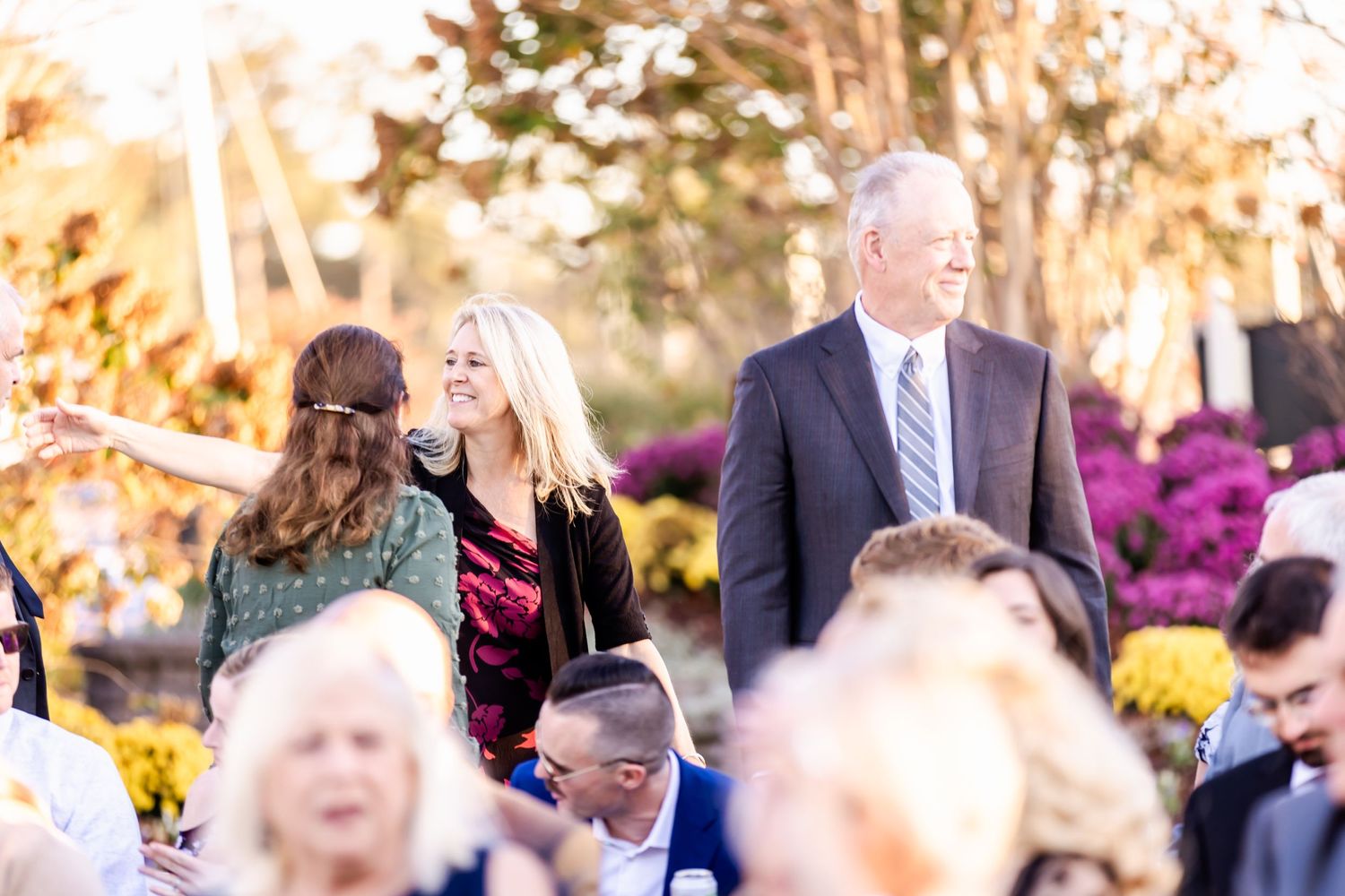 Outdoor event guests mingle during golden hour with colorful autumn flowers in the background.