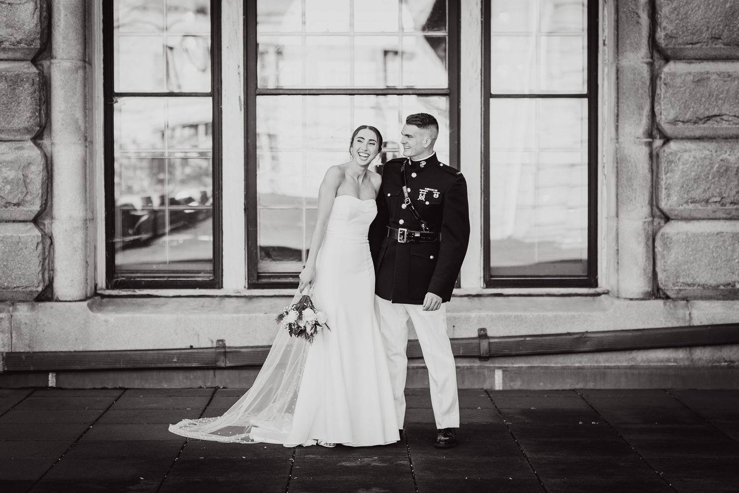 A timeless black and white wedding portrait of a couple standing in front of a historic stone building.