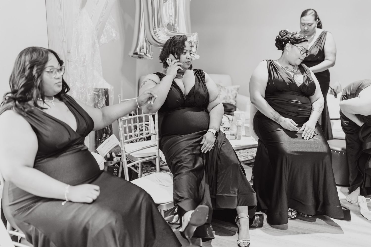 Wedding party members in dark formal dresses gather in a candid black and white moment.