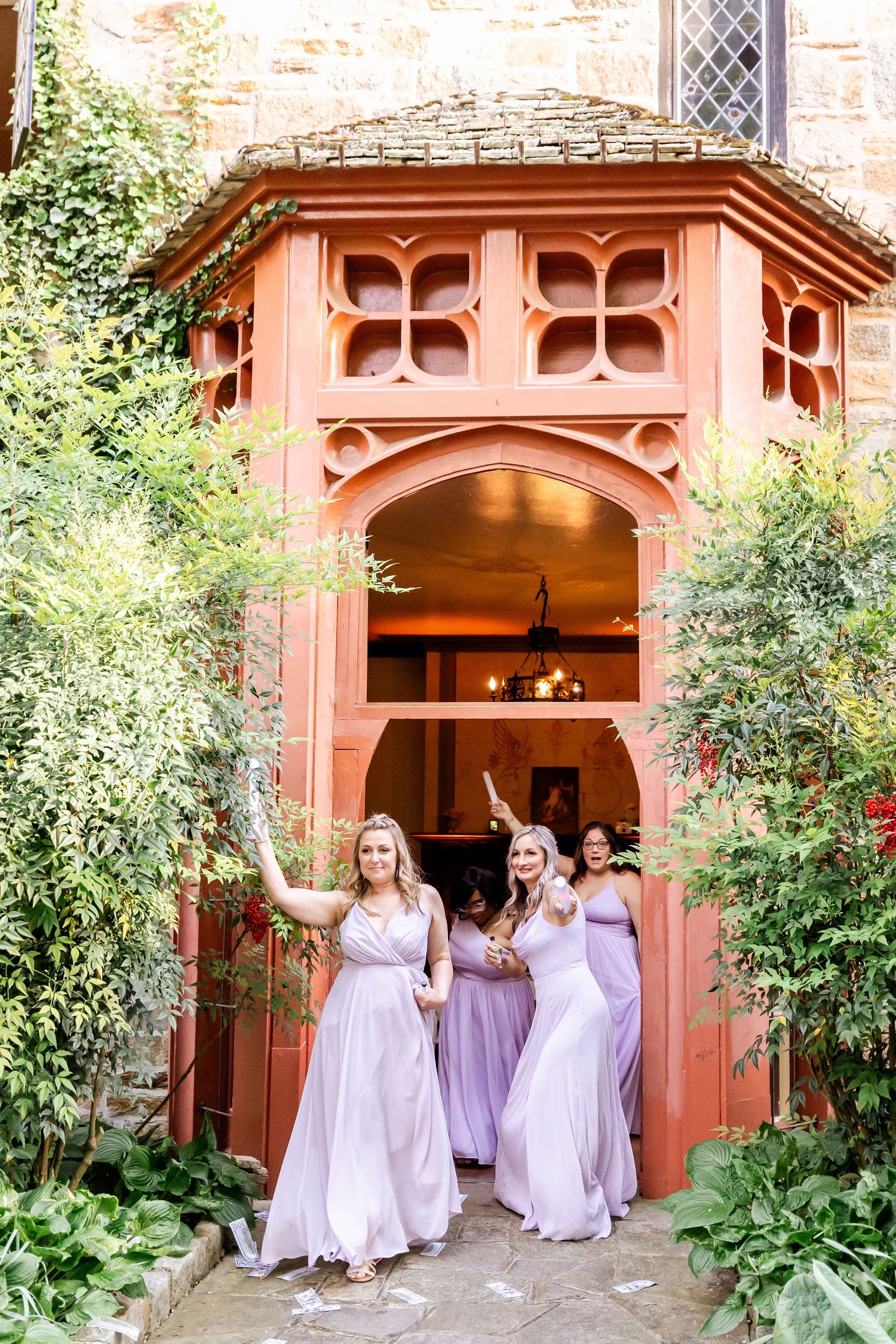 Bridesmaids in lavender dresses exit through a decorative terracotta archway surrounded by greenery.