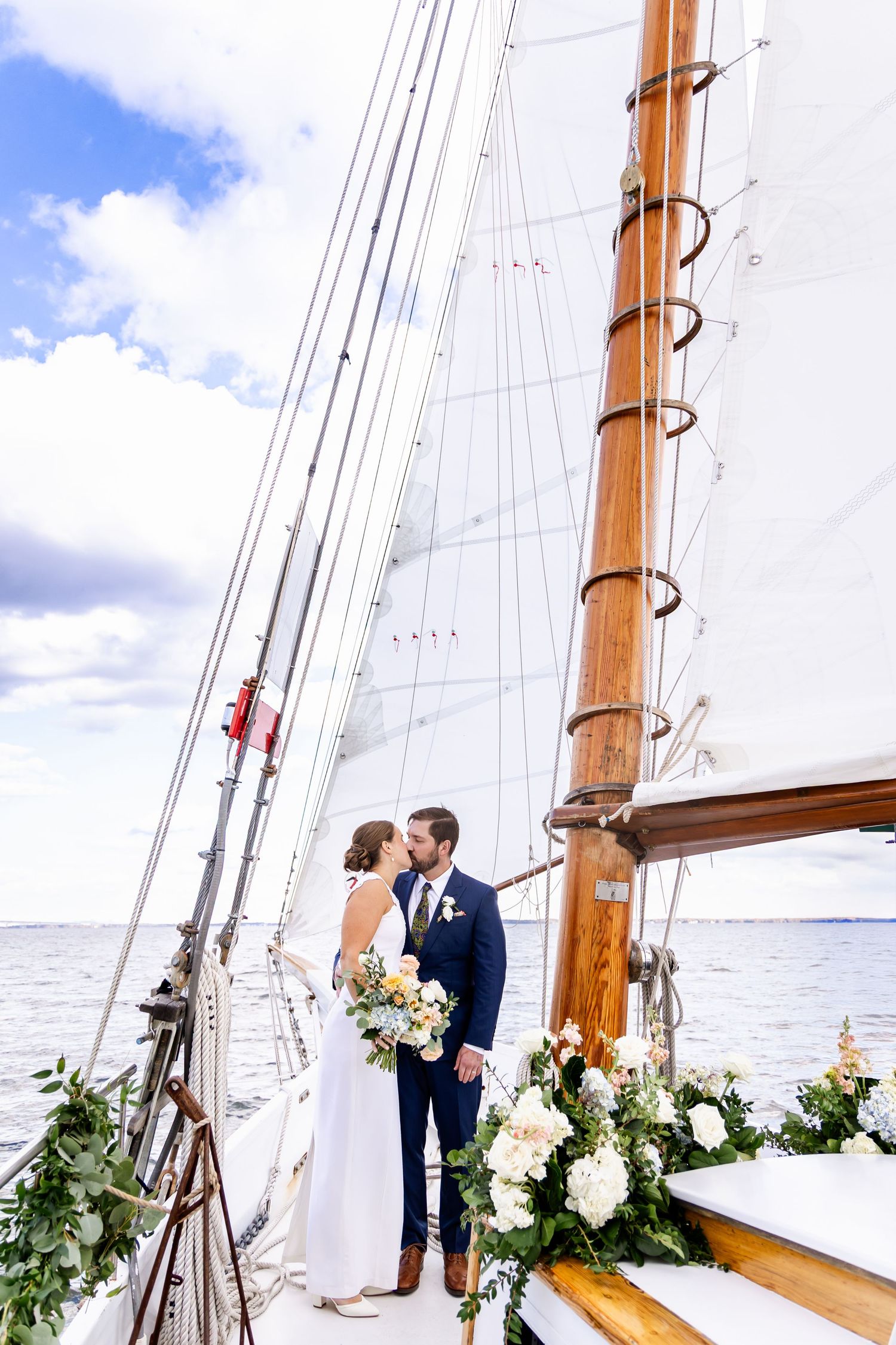 A romantic wedding moment aboard a classic sailing yacht decorated with white floral arrangements and greenery.