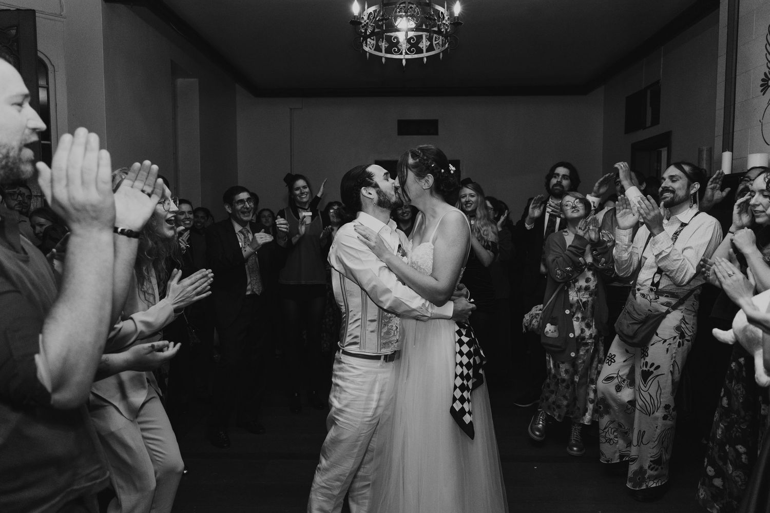 Black and white photo of guests dancing and celebrating at a wedding reception on a dance floor.