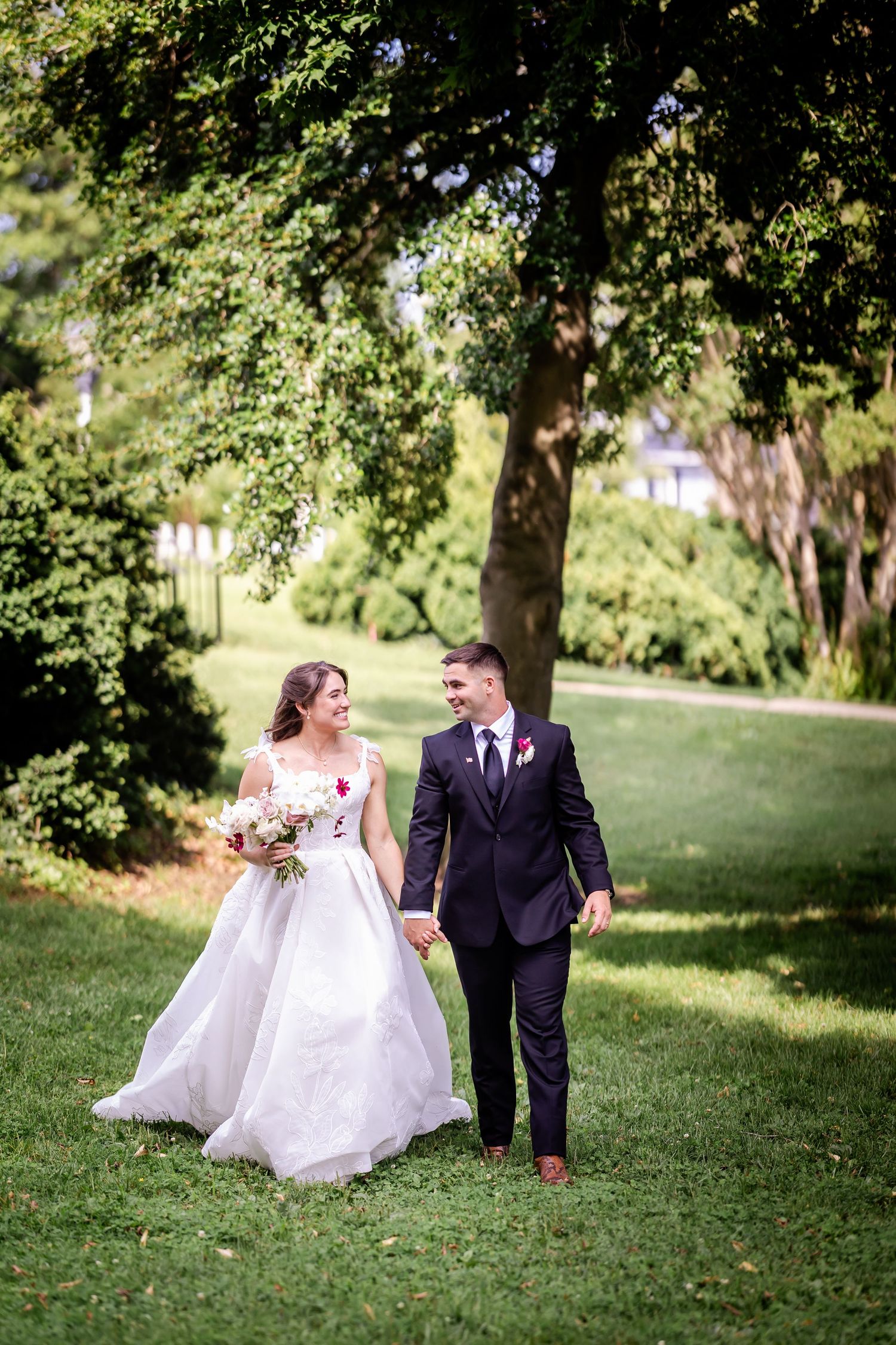 Newlyweds walking hand in hand through a lush green garden setting.