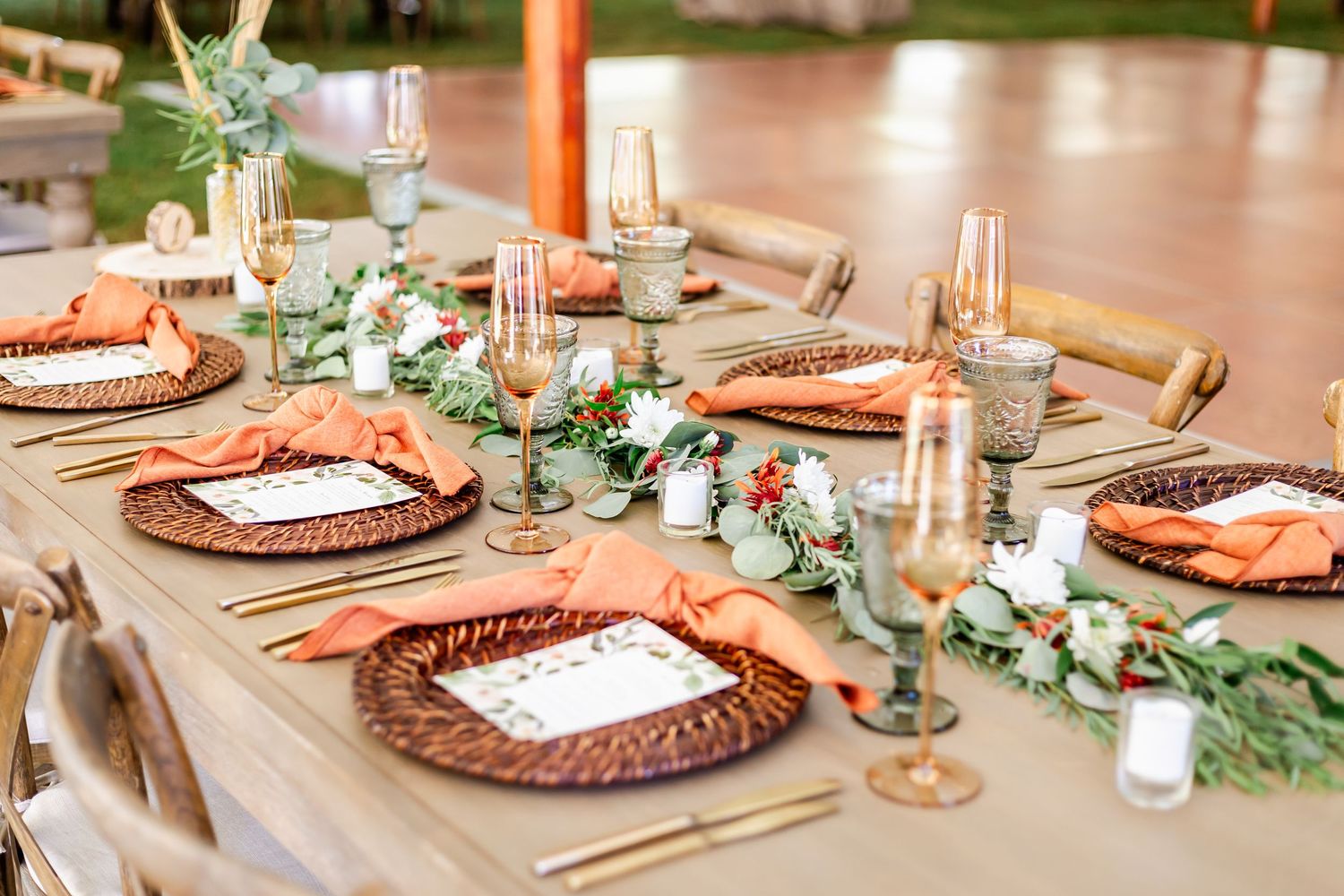 Wedding reception tablescape with copper chargers, coral napkins and eucalyptus garland runners.