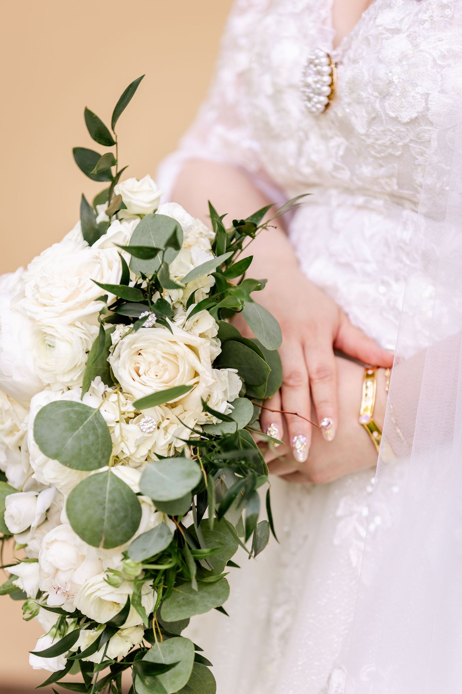 Close-up of a white rose and eucalyptus bridal bouquet with the bride's hand displaying wedding rings.