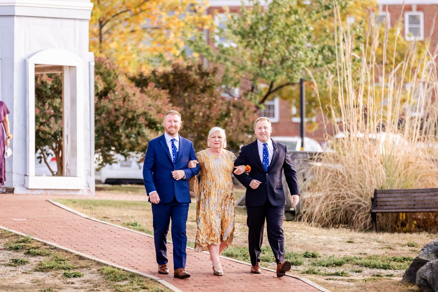 Wedding party walking along autumn garden path with golden decorative grasses.