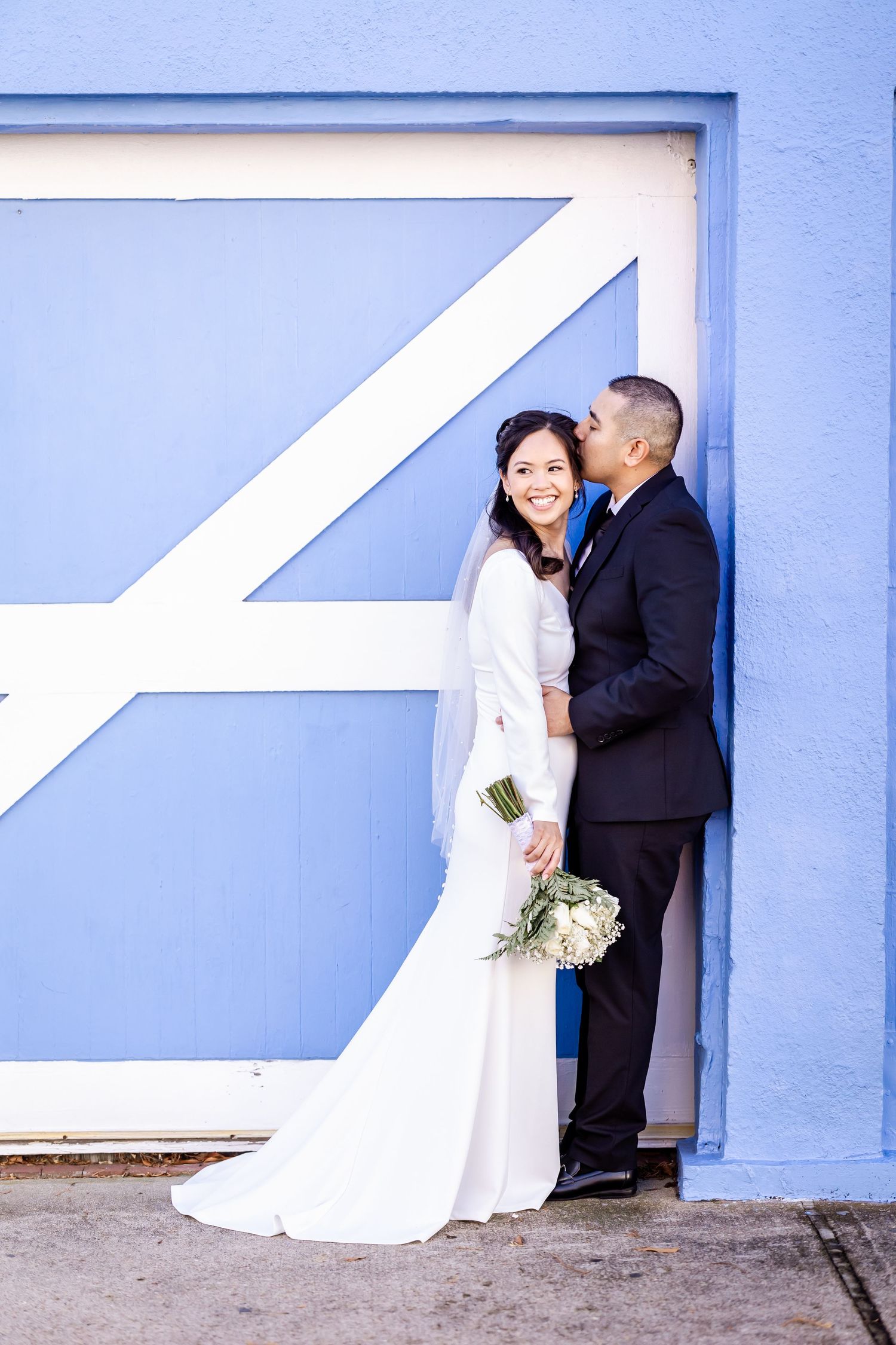 Wedding couple shares an intimate moment against a blue wall with white geometric designs.