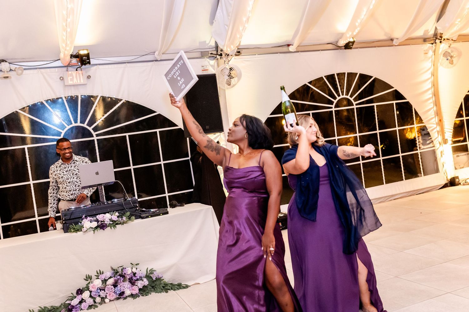 Wedding reception dance party in full swing under an elegant white tent with purple decor.