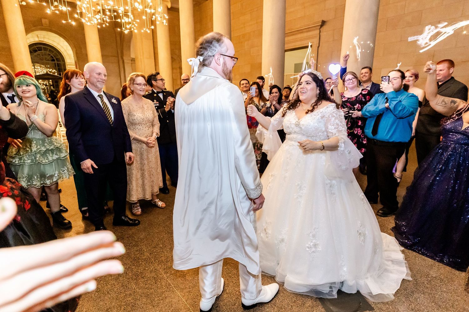 Wedding celebration with guests gathering around the couple in a grand columned hall.