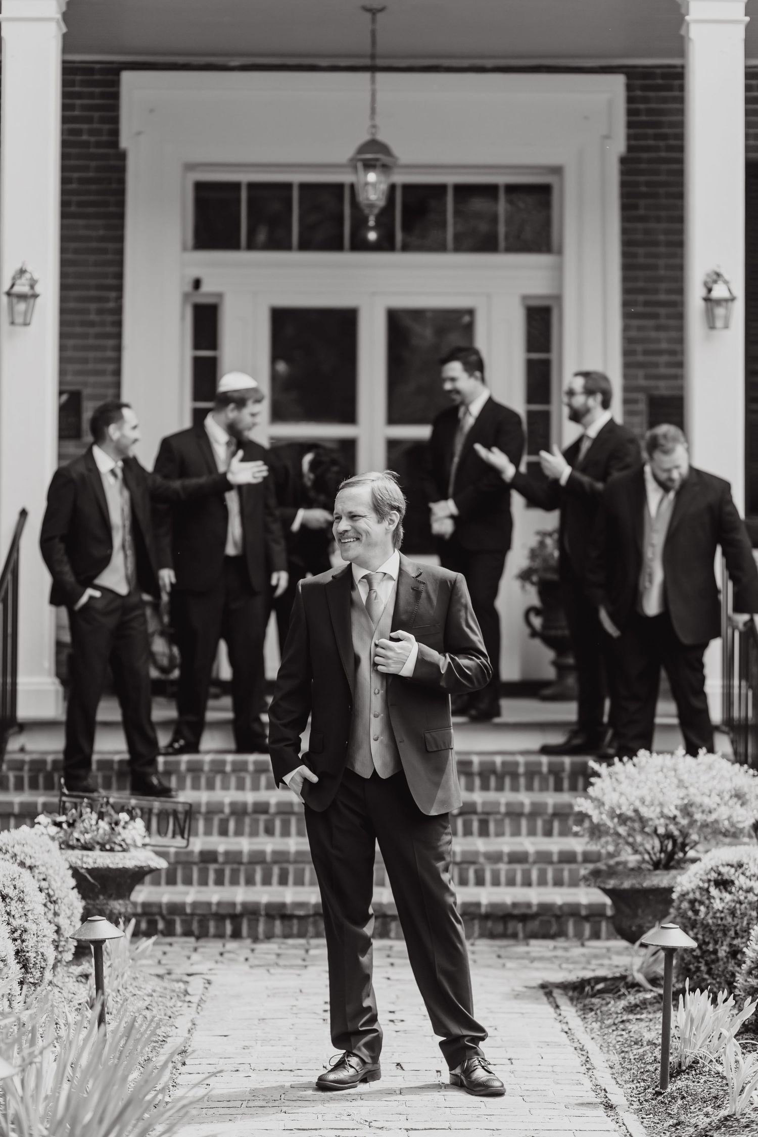 Black and white photo of groomsmen in formal suits gathered outside a grand entrance with brick steps and white columns.