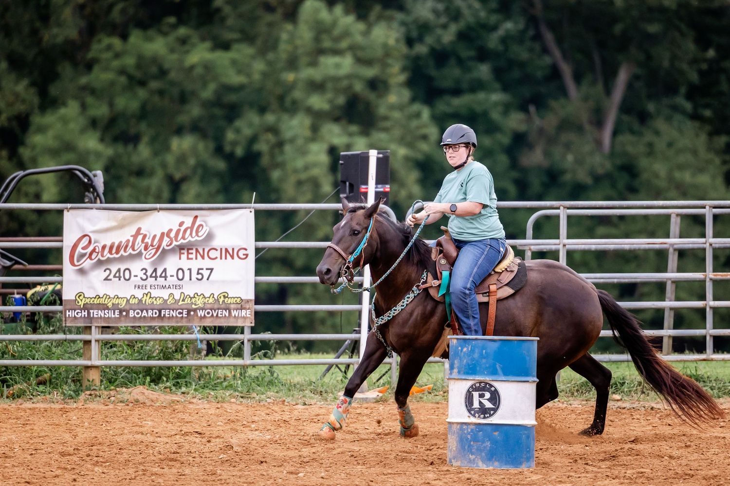Barrel racing competition at a countryside arena with rider navigating blue barrel.