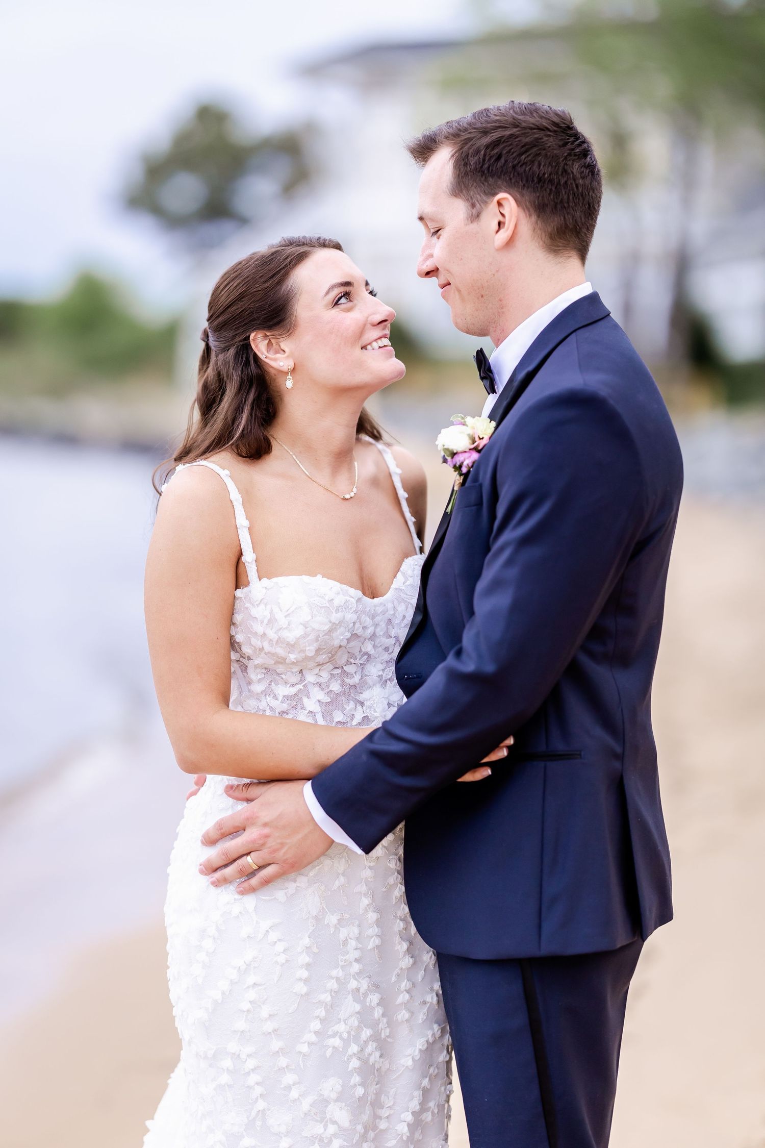 A joyful couple in wedding attire embrace and laugh together by the water.