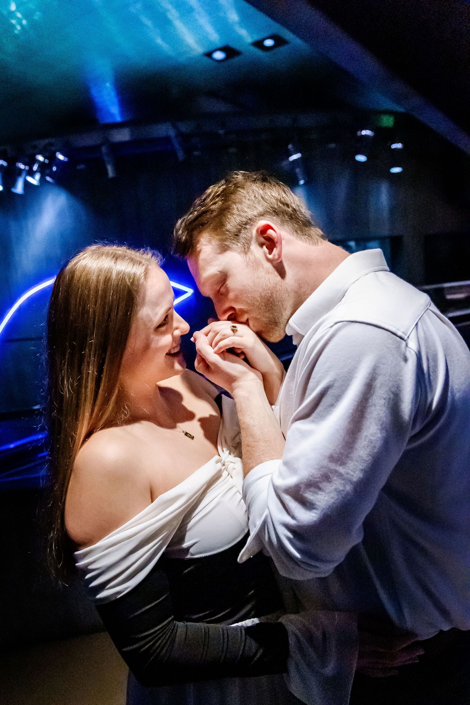 A romantic couple dancing together in an intimate moment under dramatic blue lighting at a venue.