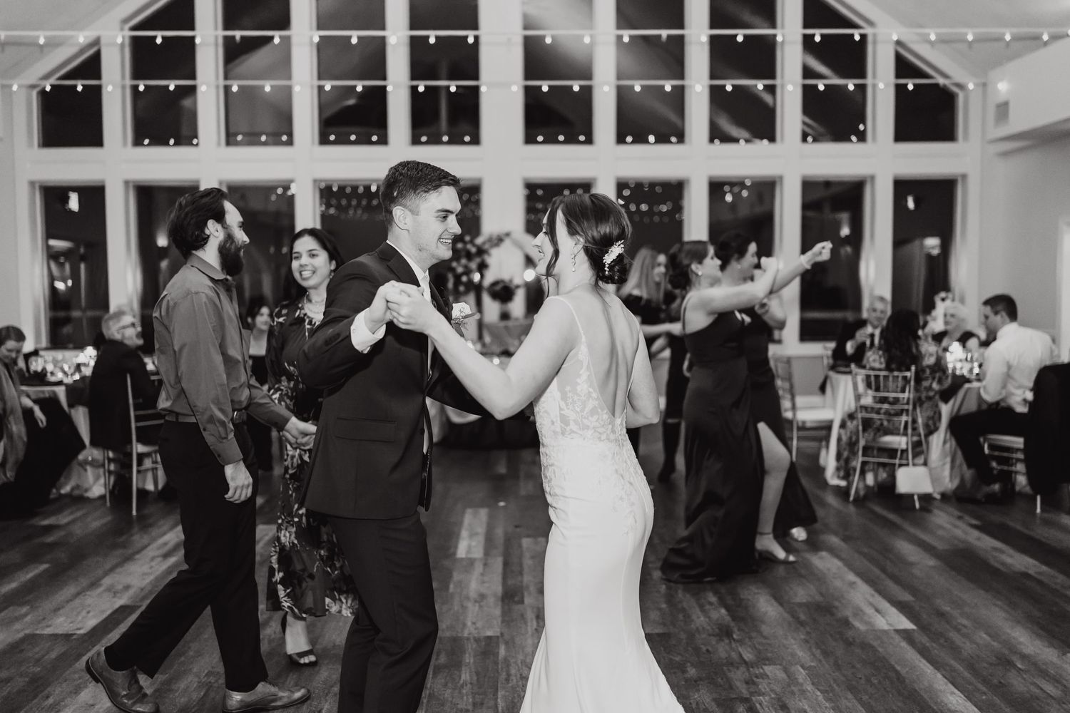 A couple dances together at an evening wedding reception with string lights and other guests in the background.