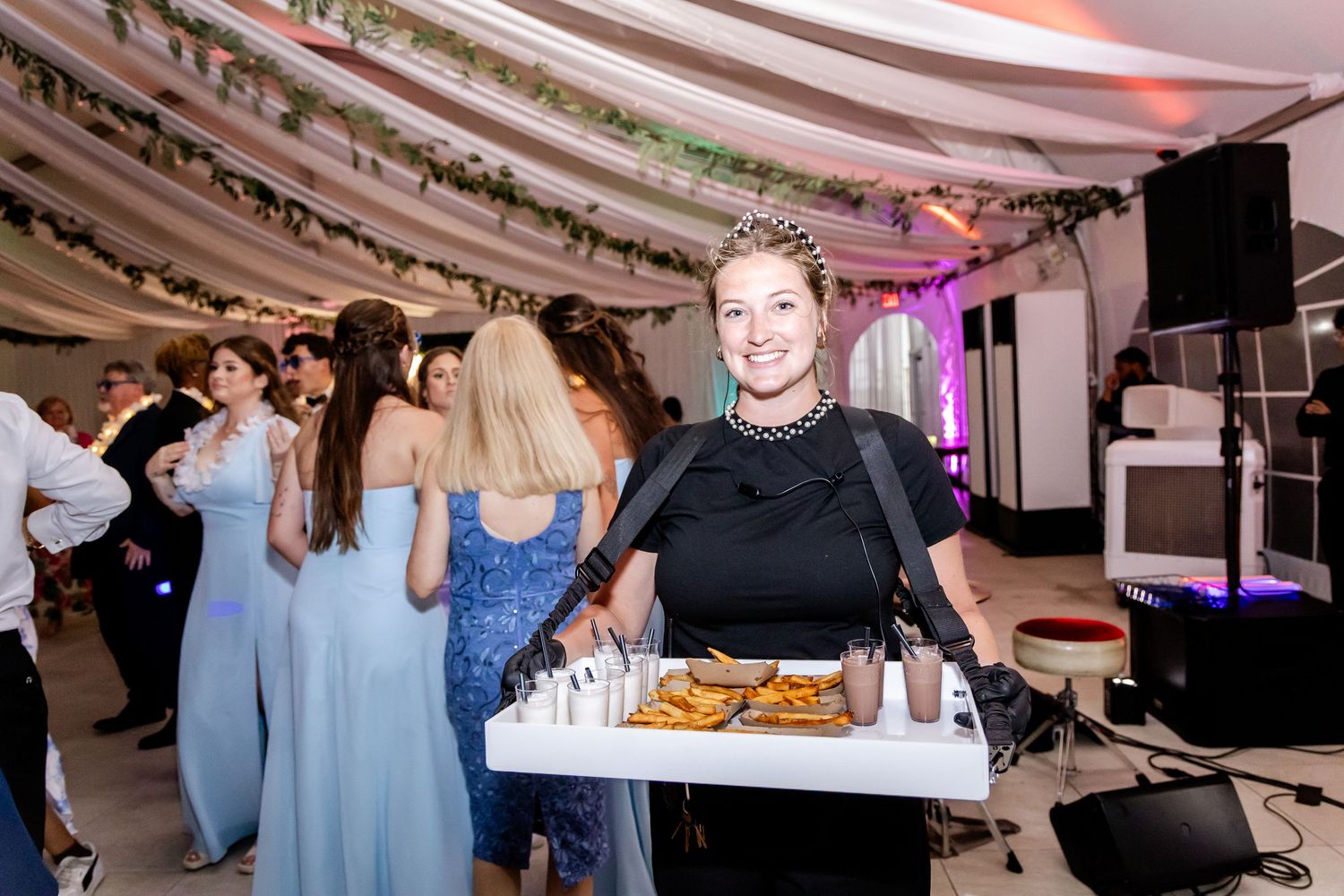 Wedding guests enjoying a lively dance party under draped fabric ceiling with colorful lighting.