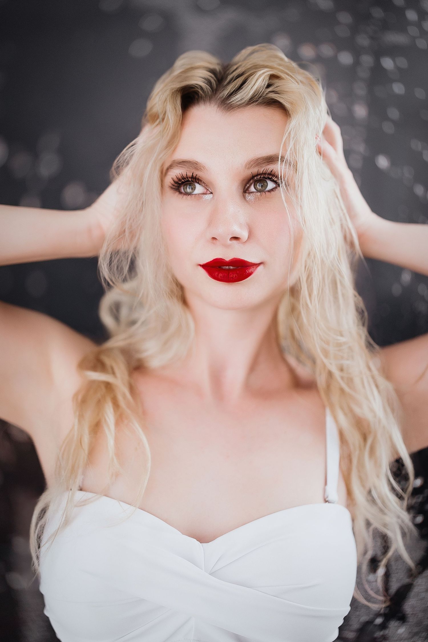A woman in a white dress poses against a dark background with sparkling bokeh lights.