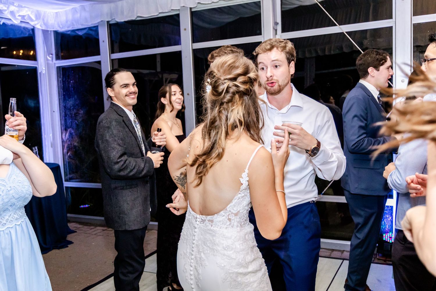 Wedding celebration with guests dancing under blue lighting in a tent venue.