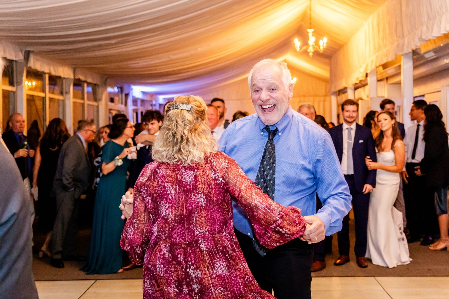 Wedding guests dance together under warm lighting and elegant draped ceiling decor.
