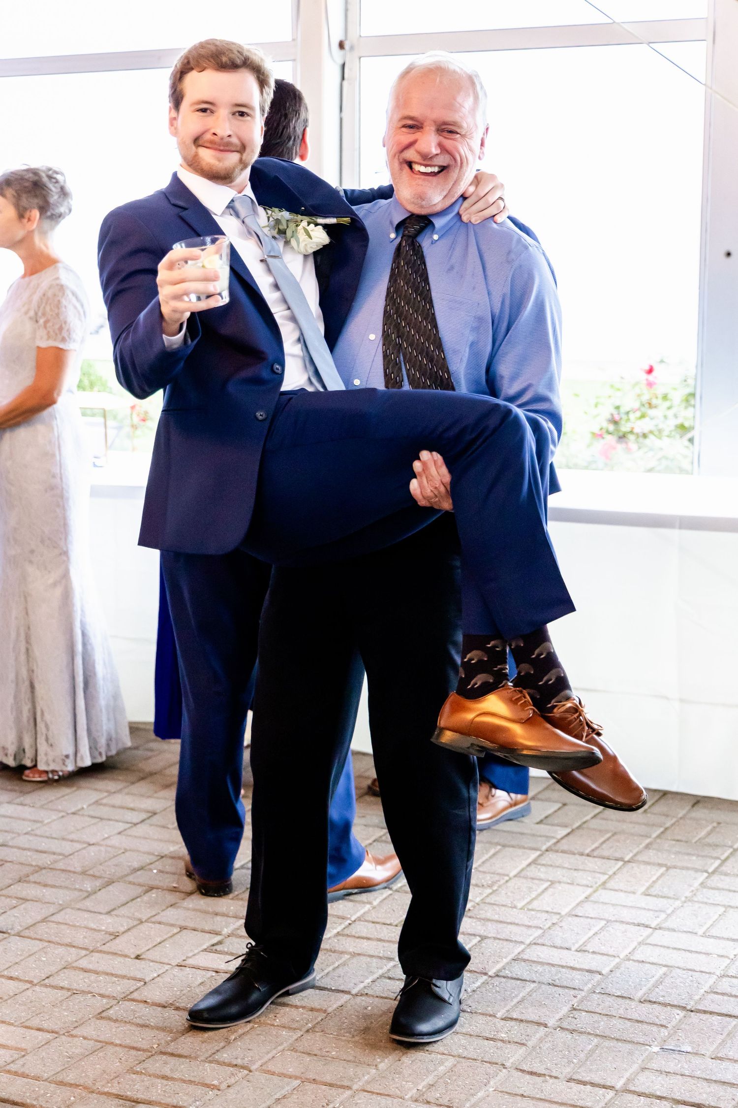 Wedding guests in suits playfully show off their colorful socks during a candid photo moment on a tiled floor.