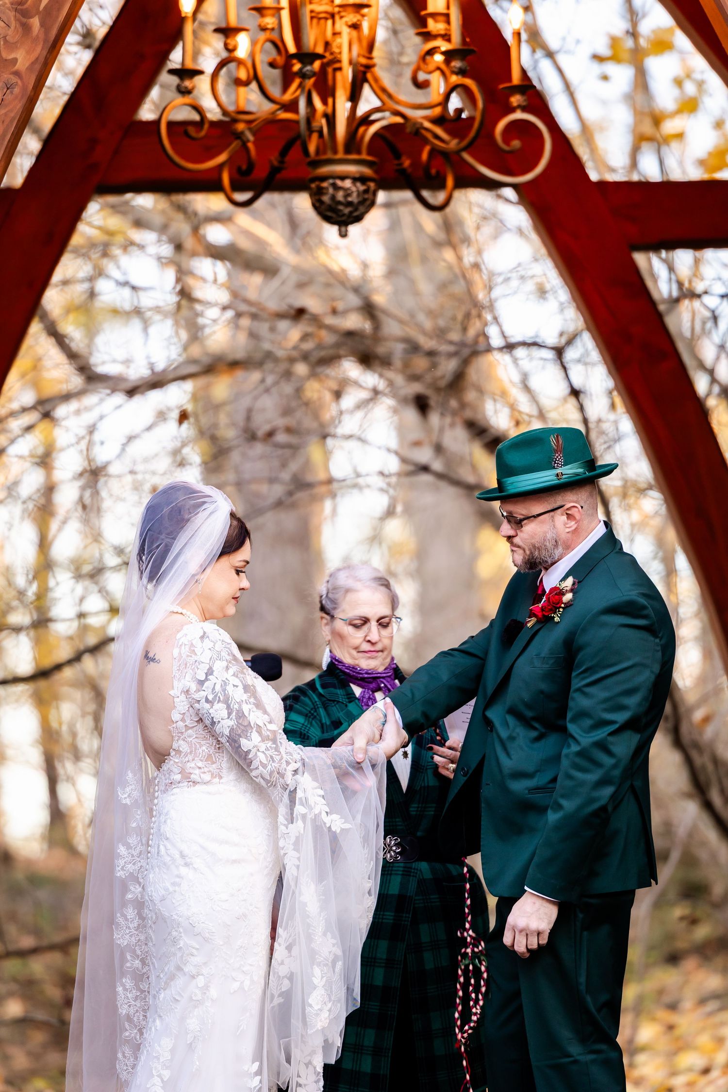 A wedding ceremony in progress under a wooden pavilion with hanging chandelier.