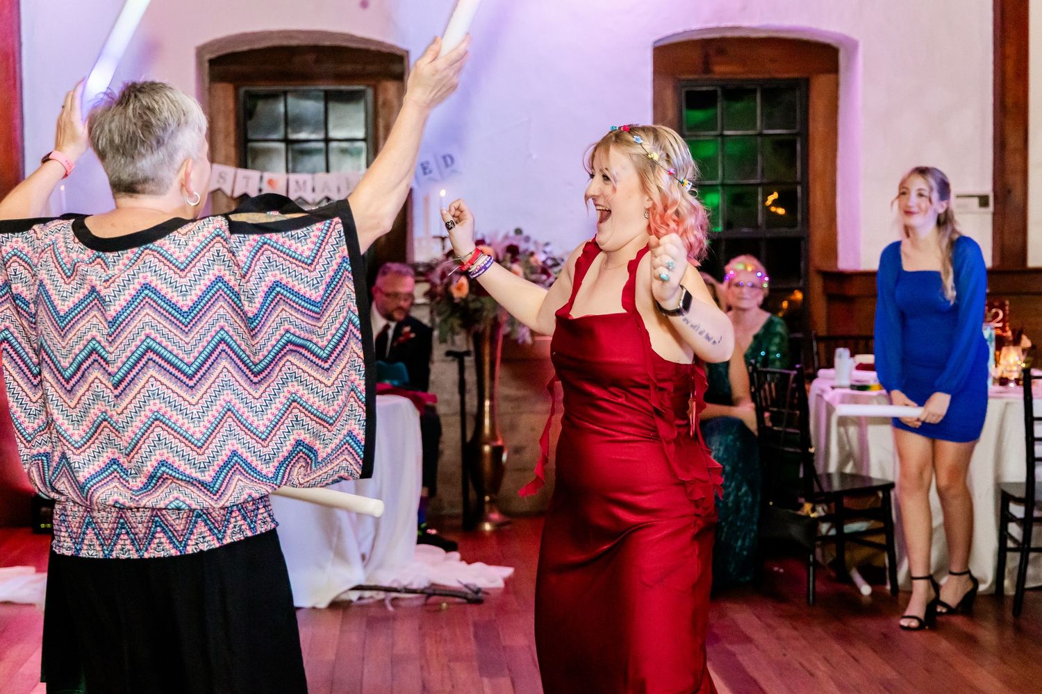 Wedding guests dancing and celebrating in colorful attire on a wooden dance floor.