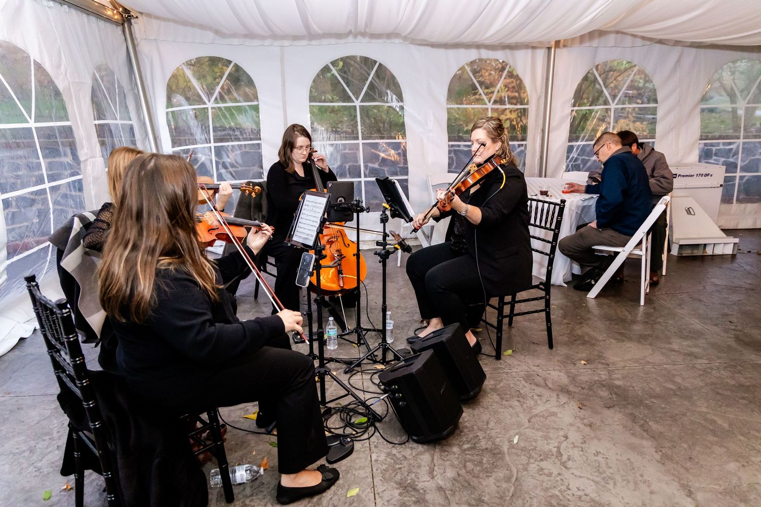 String musicians perform in a white tent during a wedding reception.