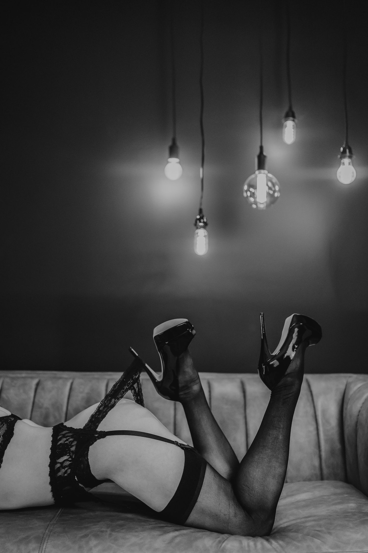 A black and white photo series showing legs in high heels on a couch beneath hanging light bulbs.