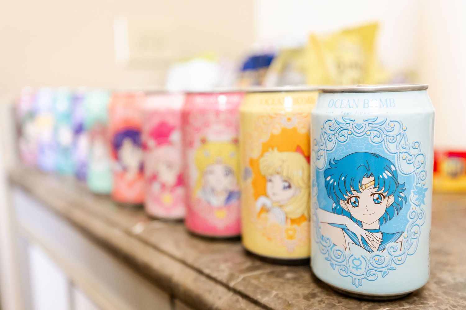 Collection of colorful anime character drink cans lined up on wooden shelf.