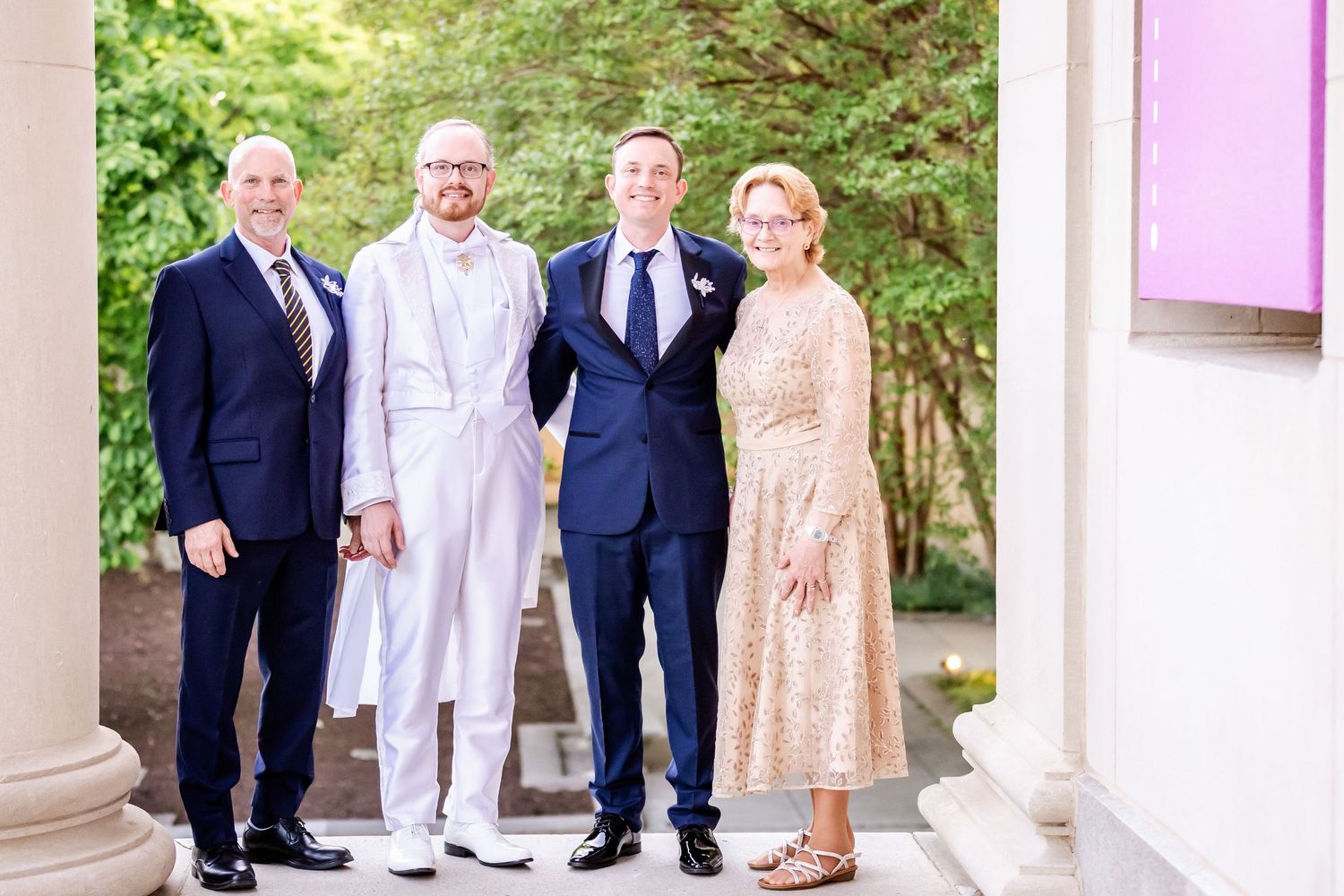 Four wedding party members pose in formal attire including white, navy, and champagne colored outfits.