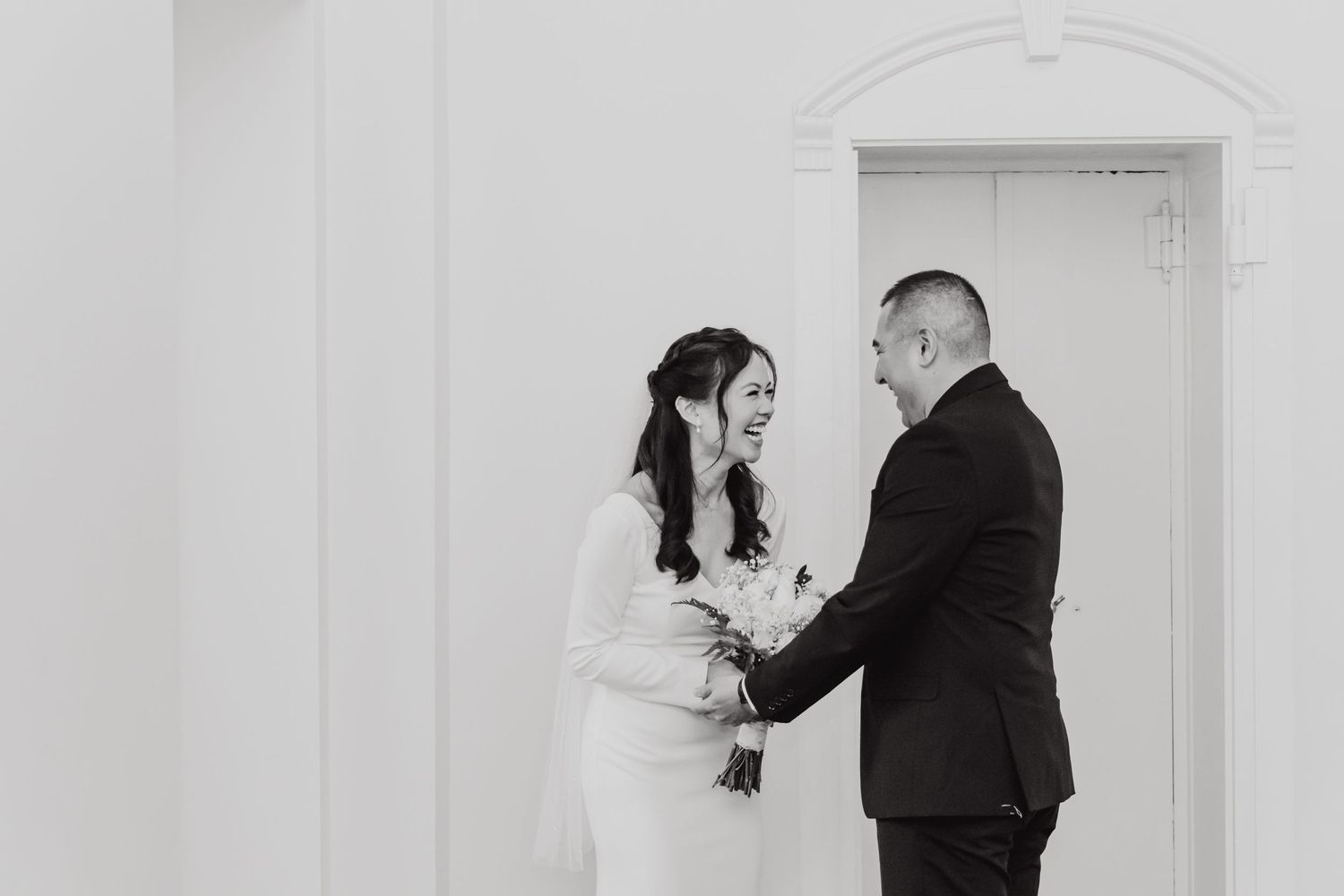 A tender black and white wedding moment captured against a minimalist white wall backdrop.