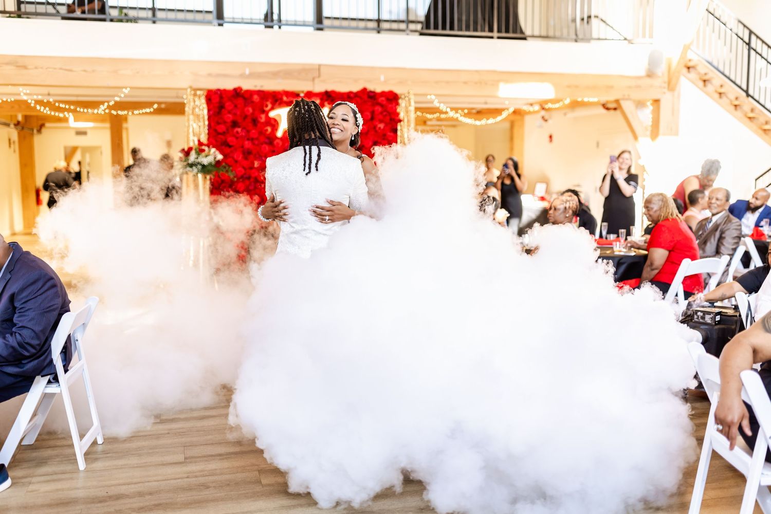 Wedding couple dances surrounded by smoke effects and seated guests at indoor reception venue.