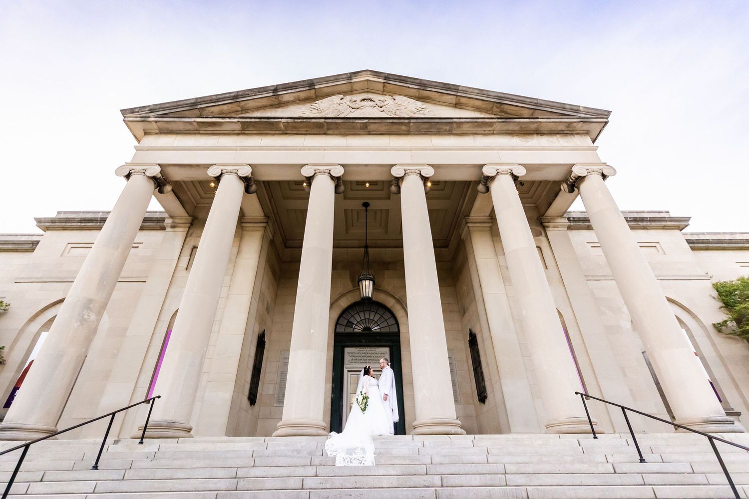 Wedding photo at neoclassical building entrance with dramatic white columns and stone steps.