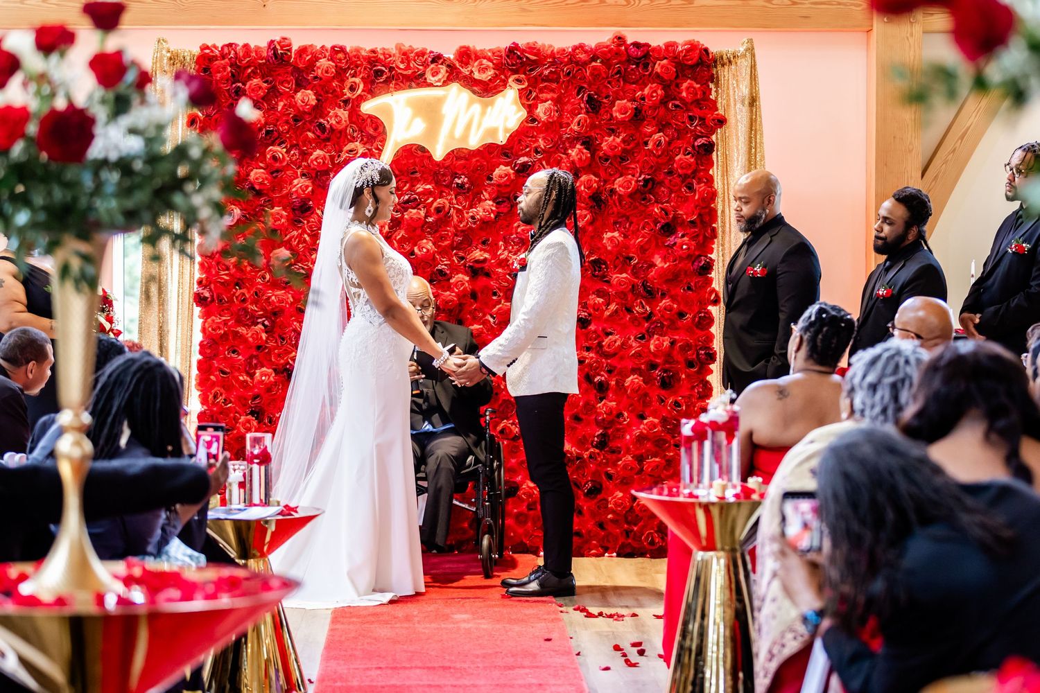 Wedding ceremony with dramatic red rose wall and guests seated on either side.