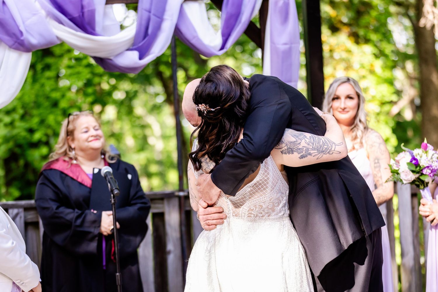 An emotional moment during an outdoor wedding ceremony under purple decorative elements.