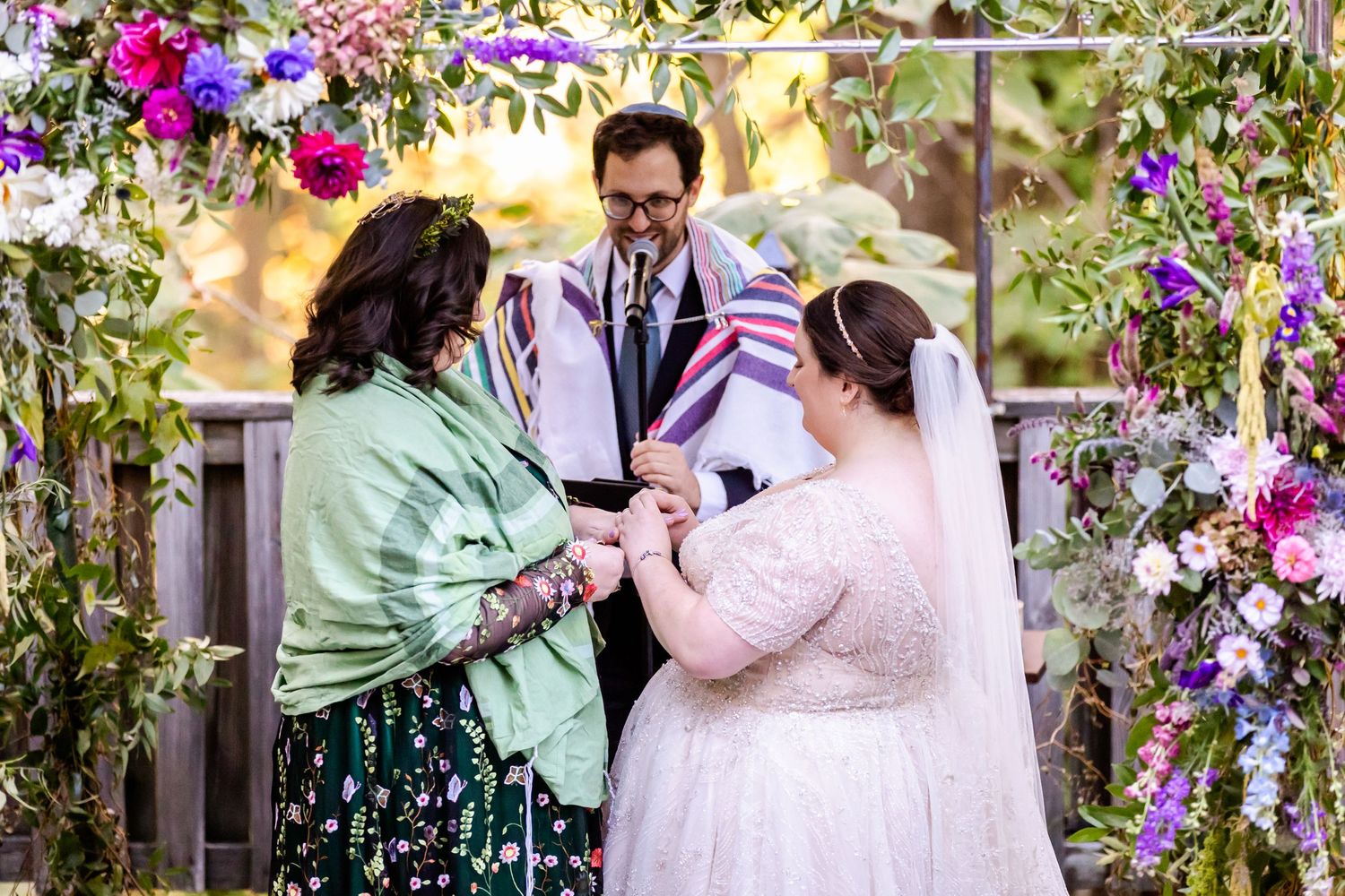 Wedding ceremony under a floral arch with vibrant purple and pink blooms.