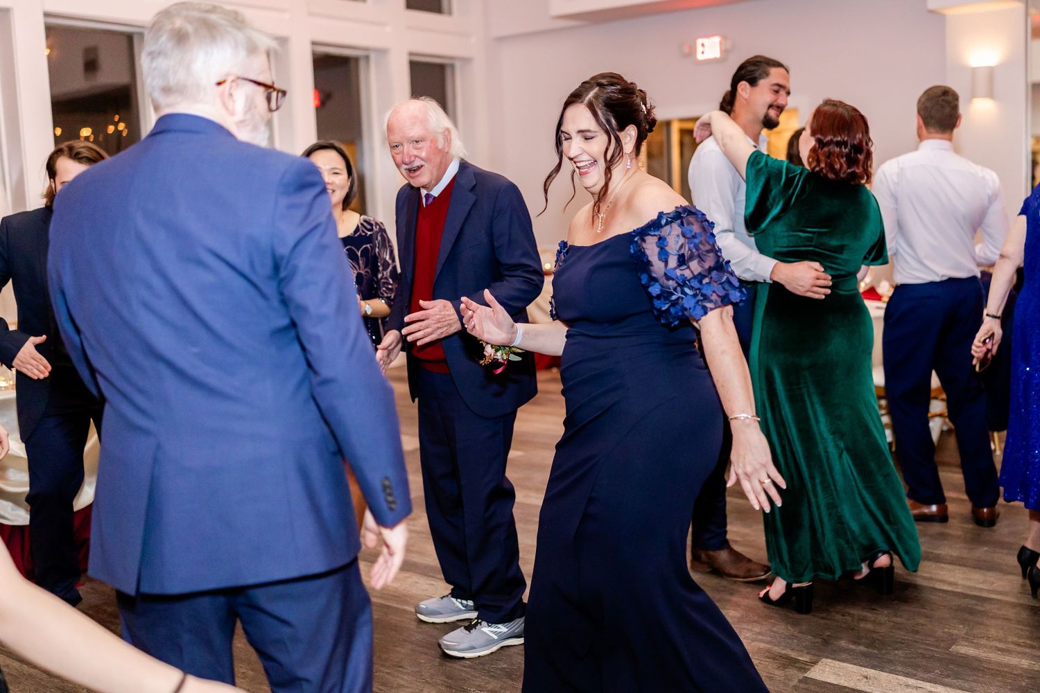 Wedding guests dancing and mingling on a spacious dance floor at an indoor reception.
