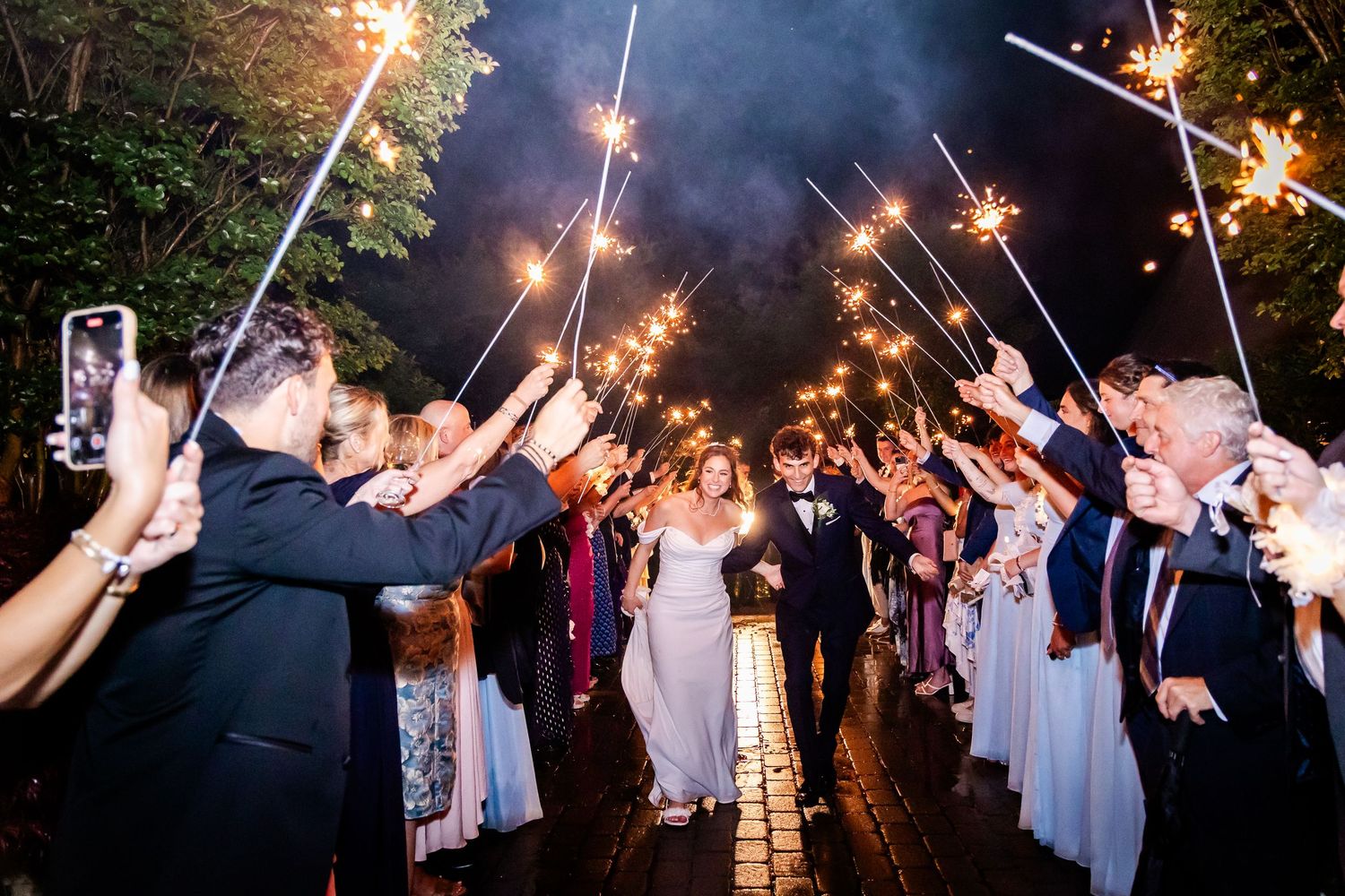 Wedding guests holding sparklers creating a magical nighttime exit tunnel outdoors.