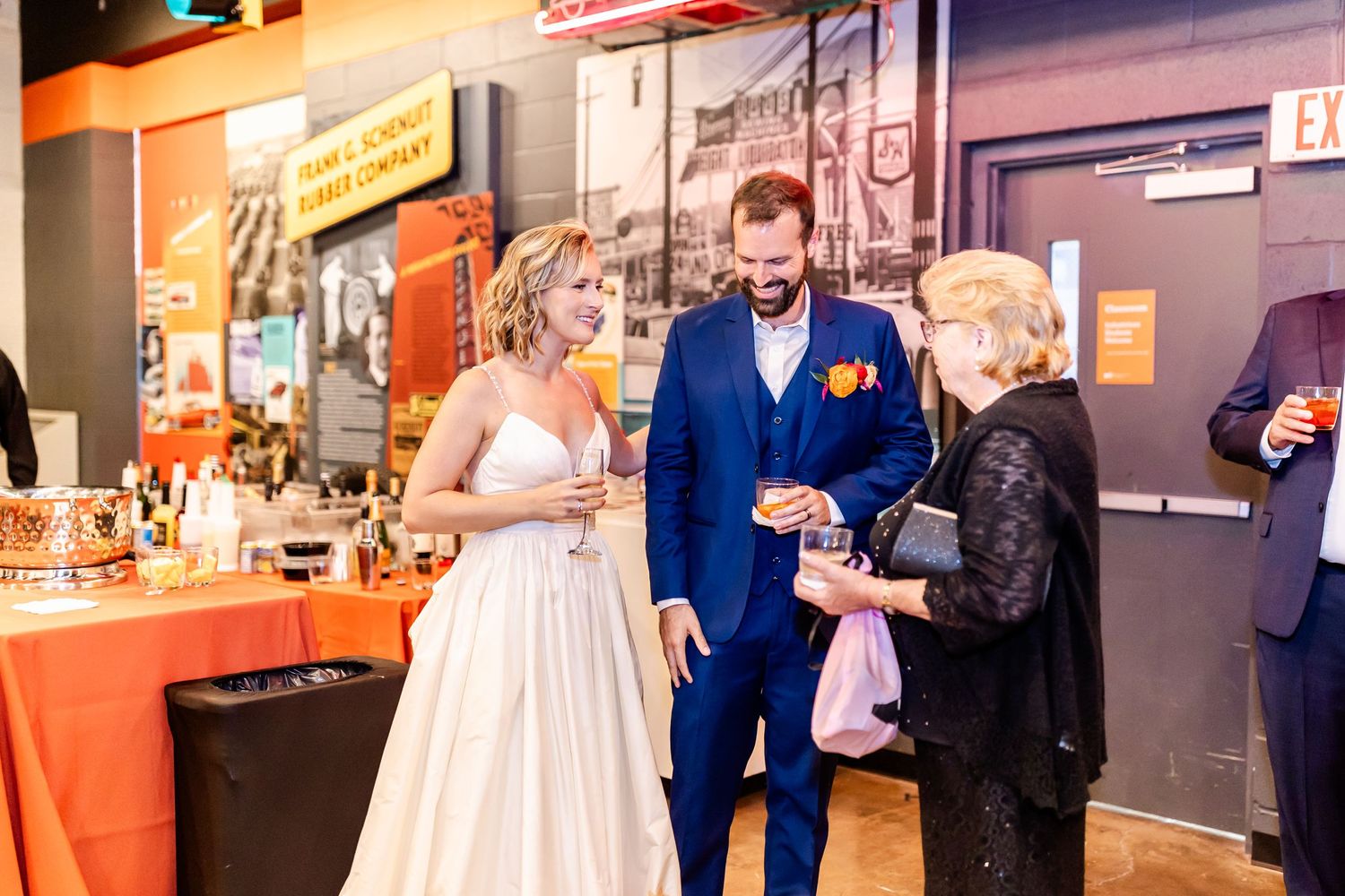 People sharing drinks and conversation at a wedding reception with orange decor details and warm lighting.