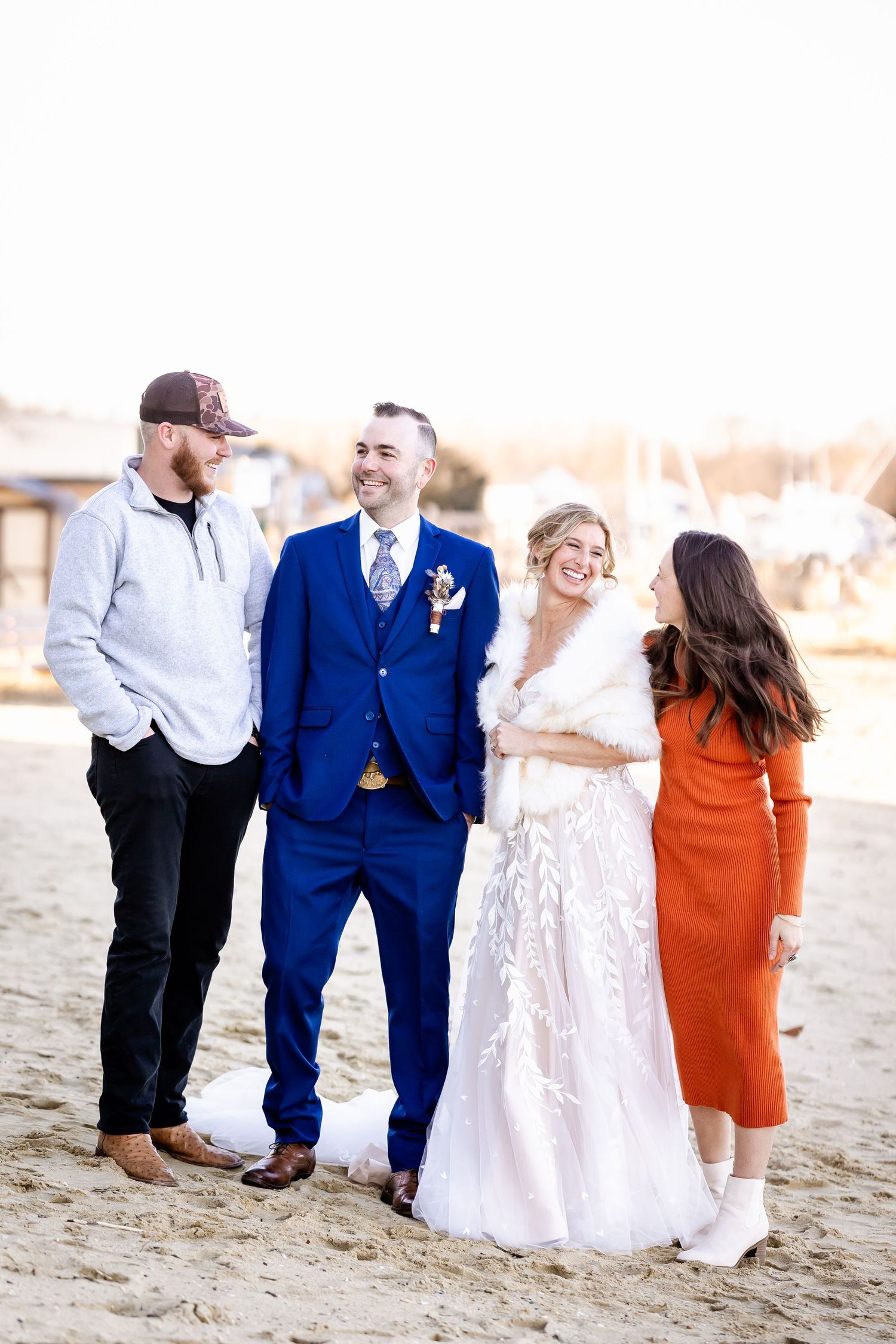 Wedding party of four enjoying casual conversation on a beach at sunset.