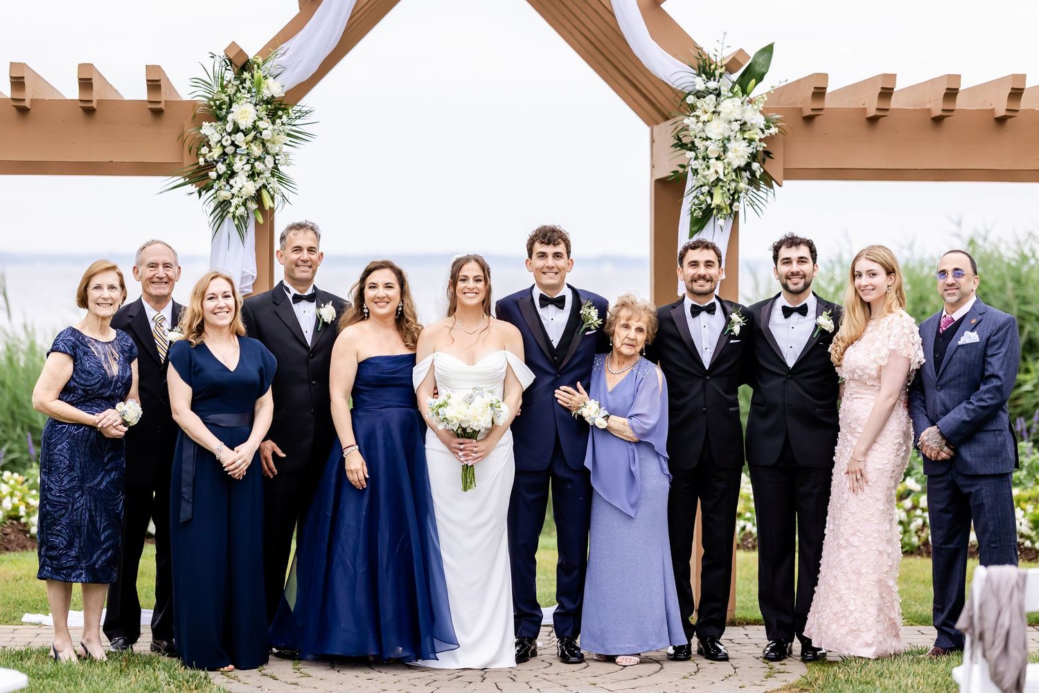 Wedding party group photo under wooden arch with floral decorations.