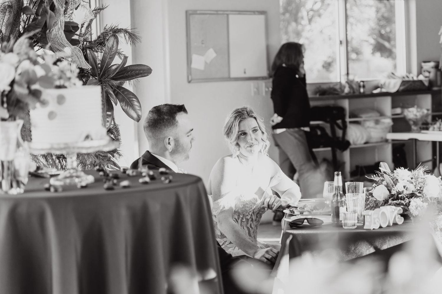 Black and white photo of guests seated at a wedding reception with floral centerpieces.