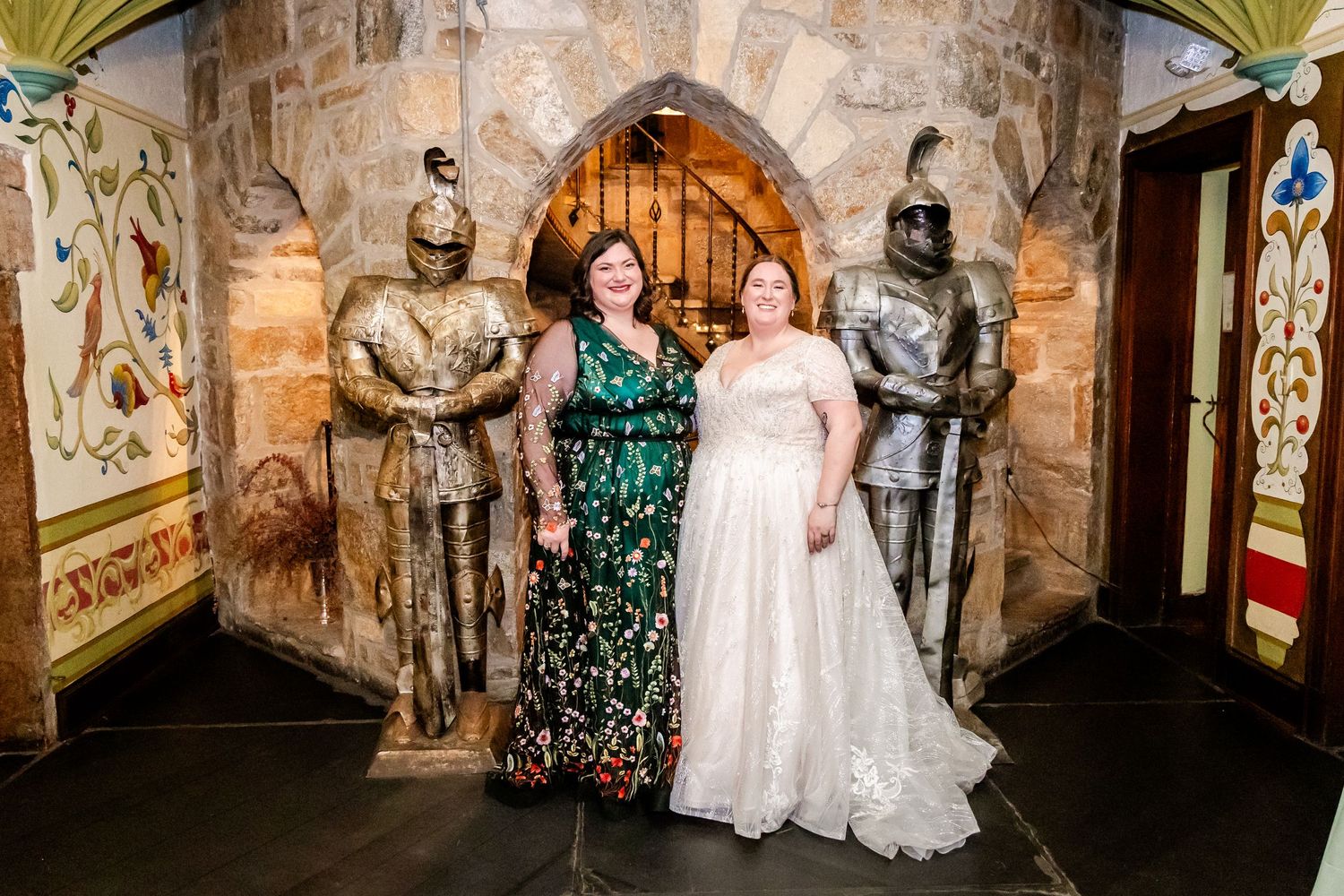Wedding party poses between medieval knight statues in a castle-like stone corridor.
