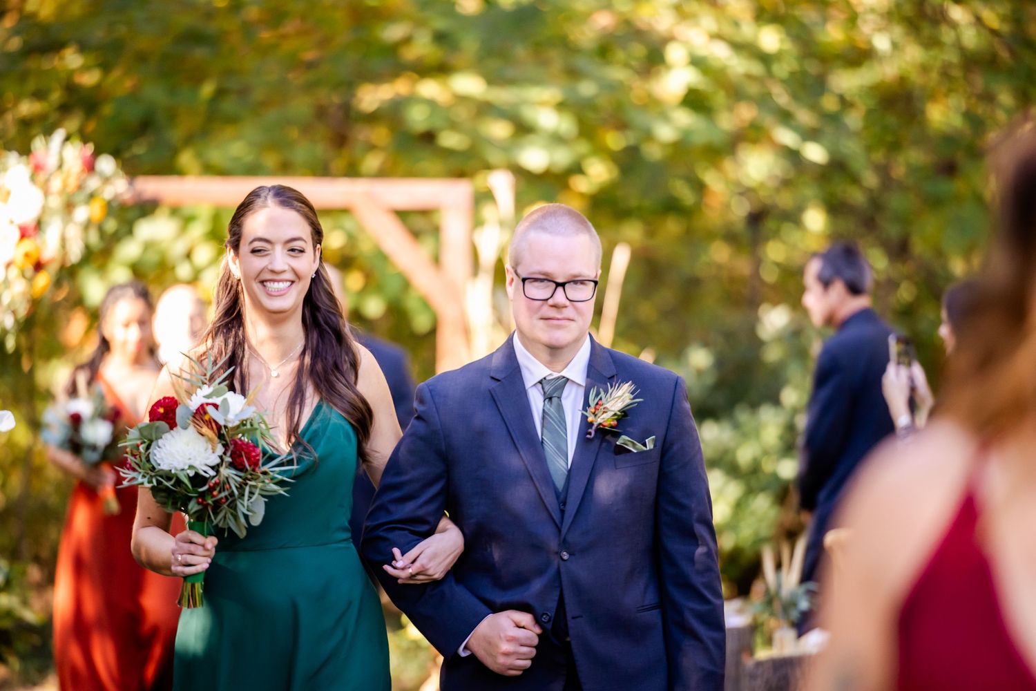 Wedding party members walk together on outdoor path during autumn celebration.