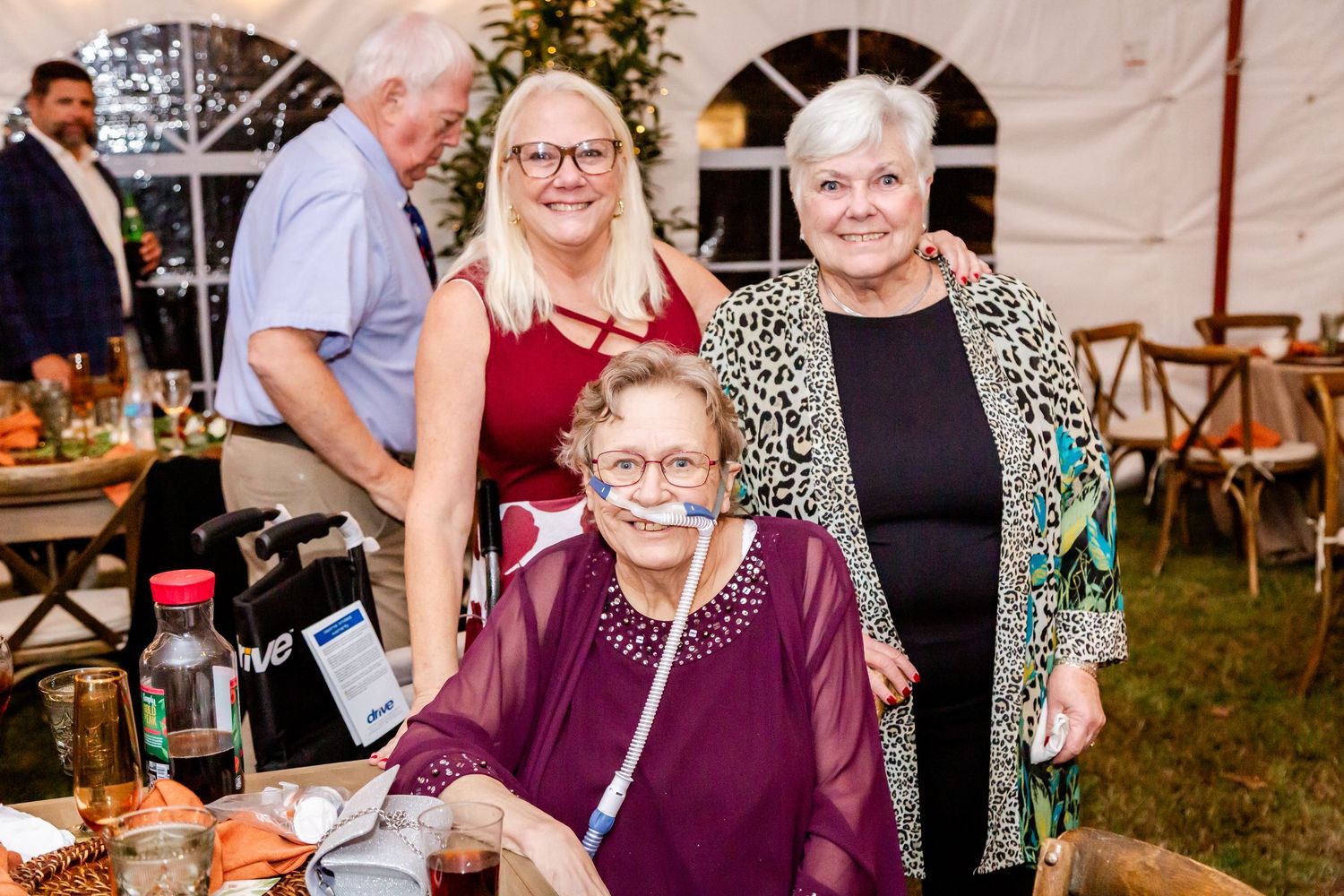 Three generations gather together at an outdoor wedding reception under a white tent with rustic decor.