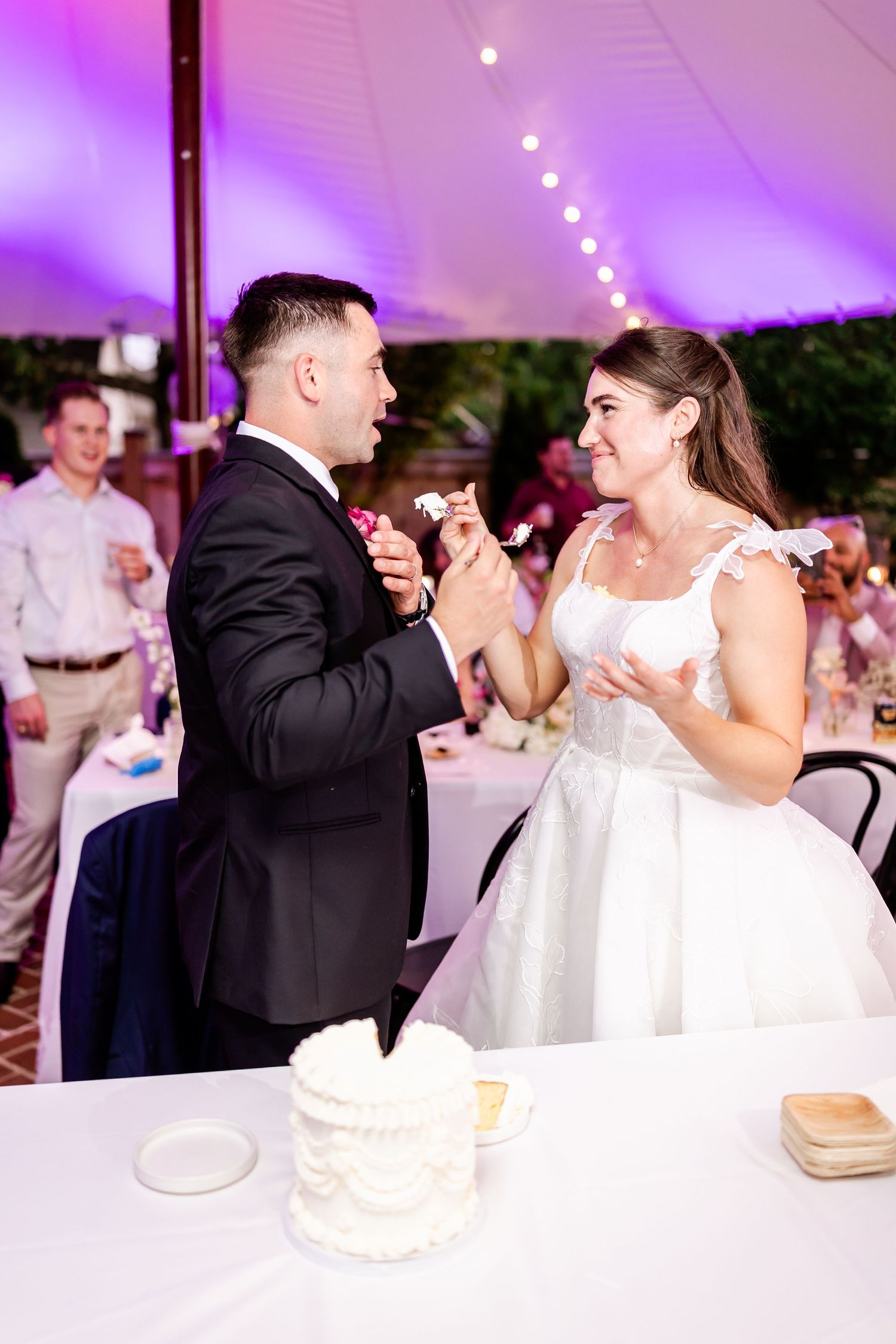 Couple shares romantic moment under purple lighting at wedding reception.