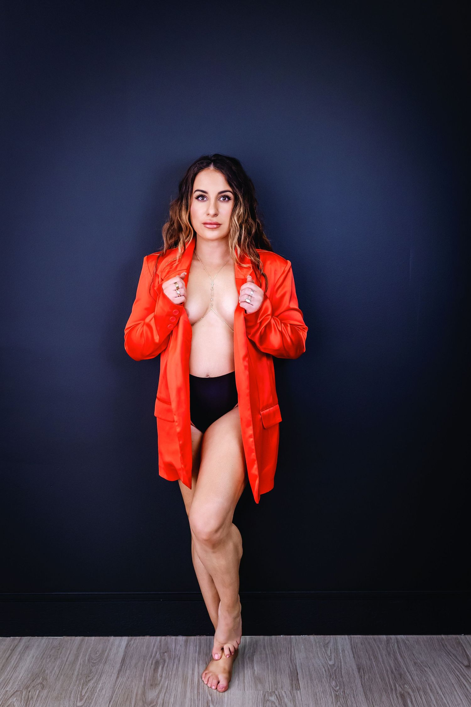 Artistic boudoir portrait featuring a vibrant red blazer against a dark blue studio backdrop.