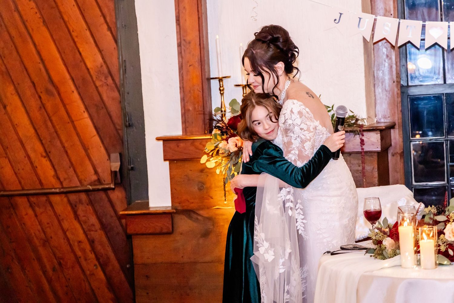 A tender embrace between two people at a wedding reception with wooden decor and floral arrangements.