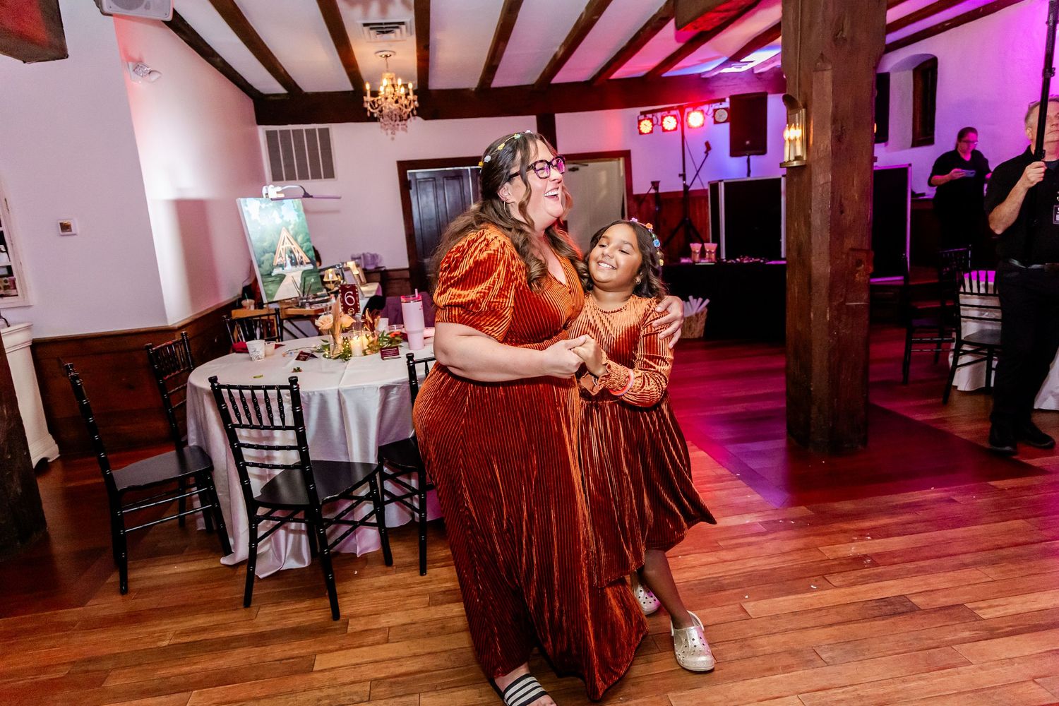 Wedding reception dance floor with pink and purple mood lighting and wooden beams.