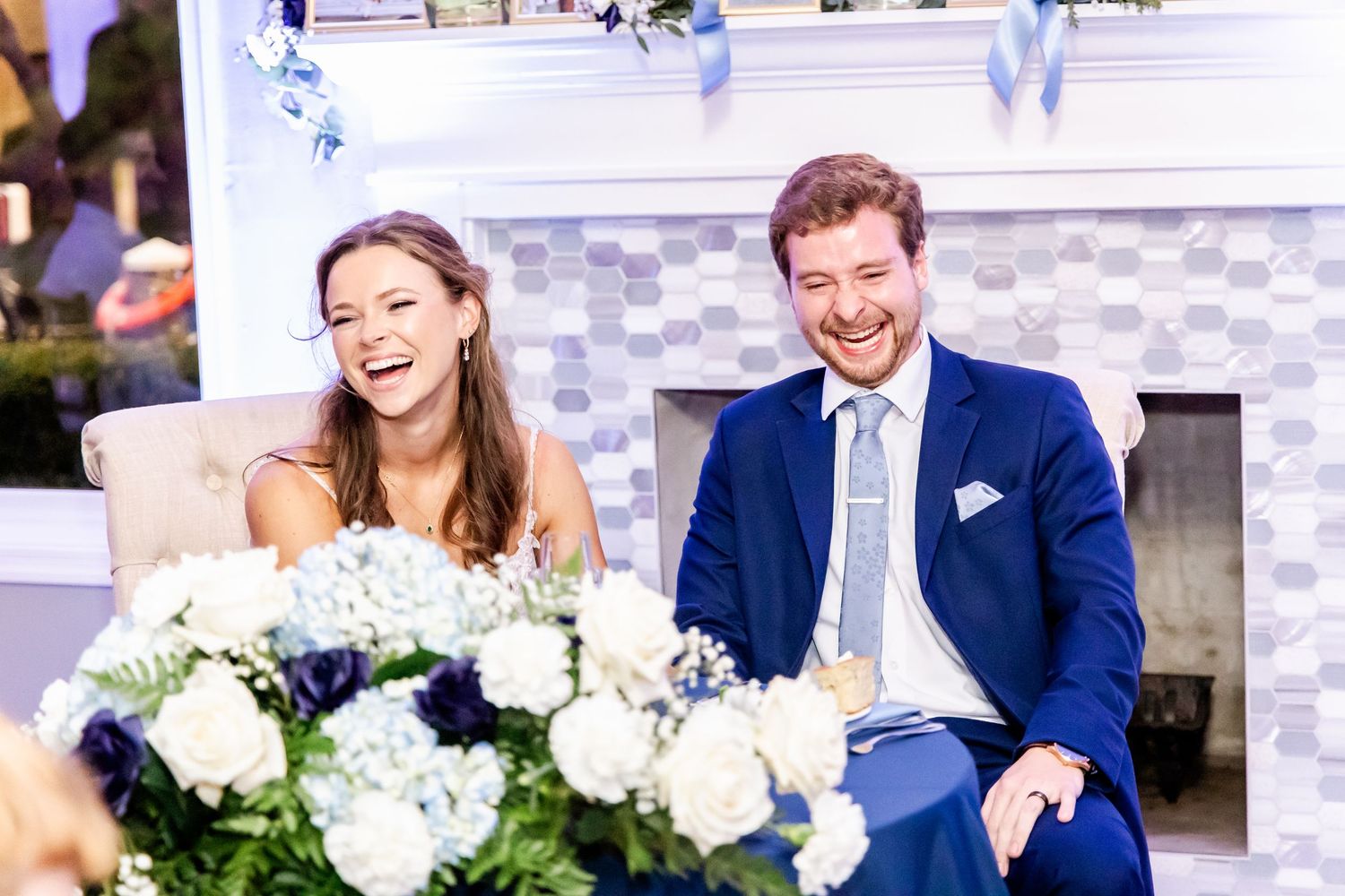 Wedding reception scene with white floral arrangements and joyful moments at head table.