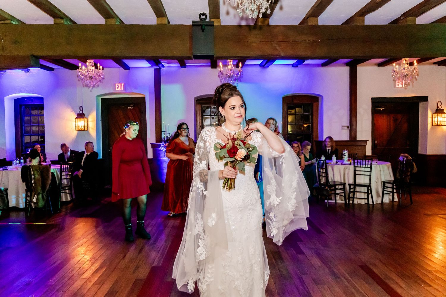 Wedding reception venue with wooden beam ceiling, chandeliers and purple accent lighting on dance floor.